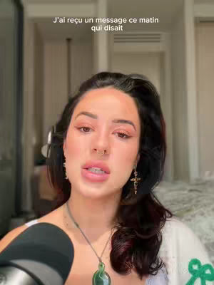 A woman with dark hair and makeup is centered in the frame. Text appears above her head. A microphone is visible at the bottom of the frame. The background is slightly blurred.