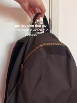 A hand holding a black backpack, hanging from a white door. Text overlayed on top in white font.
