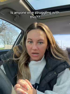 A woman is sitting in the driver's seat of a car, looking towards the camera with a concerned expression. Text overlay asks, “Is anyone else struggling with this??” The background is blurred, suggesting they are possibly outdoors.
