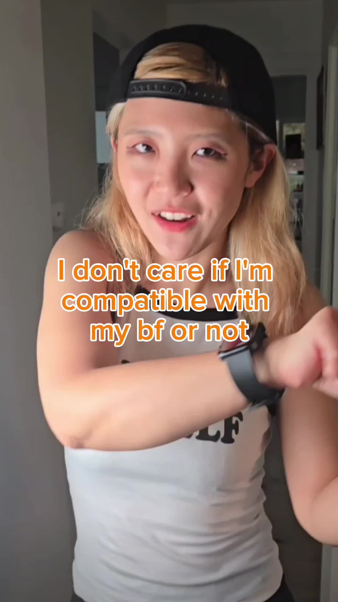 A woman in a black cap and white tank top poses, with overlaid text in the center. The background is blurred, suggesting an indoor setting.