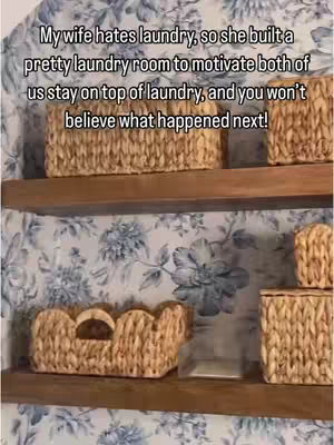 The image is of a laundry room with several wicker baskets on wooden shelves against a floral wallpaper backdrop. The top shelf holds three baskets, while the second shelf features a single basket with a cut-out handle. The wallpaper is white with blue floral pattern. The lighting appears to be natural.