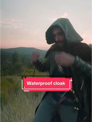 A man wearing a hooded cloak stands in a grassy field, with a red and white text overlay on the bottom.