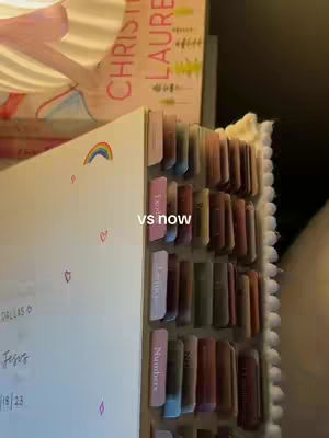 A side view reveals an open notebook with tabs, decorated with small rainbow stickers and hearts. The text "vs now" is overlaid. Behind it lies a book with a pink cover and the title "CHRISTINA LAUREN".