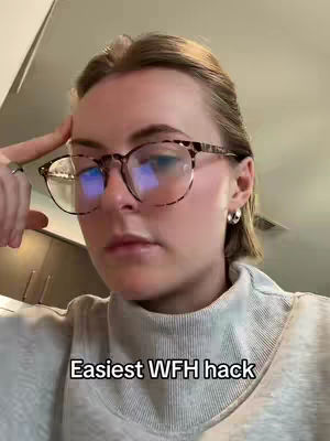 A woman with short hair and glasses is shown. She is wearing a light-colored turtleneck sweater, and has one hand raised to touch her temple. Below her, the text overlay 'Easiest WFH hack' appears.