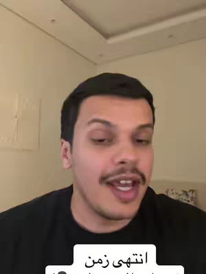 A selfie-style video cover image featuring a man with dark hair, a mustache, and a black shirt. He is looking directly at the camera with an open mouth, as if speaking. Below his face is a white rectangular overlay with Arabic text.