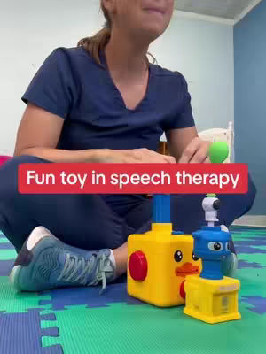 A woman is seated on a colorful patterned mat, with two toy structures in front of her. Text overlayed on a red bar reads 'Fun toy in speech therapy'.
