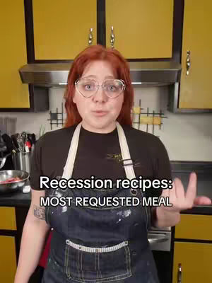 A woman with red hair and heart-shaped glasses stands in a kitchen, arms slightly outstretched, with text overlayed on the image.