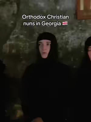 The image shows a group of Orthodox Christian nuns. The nuns are dressed in black habits that cover their heads and bodies. They are standing indoors against a blurry background. The text overlay reads, "Orthodox Christian nuns in Georgia".