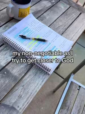 An overhead shot shows a wooden table with a notebook and pen, along with a coffee mug. The notebook is open with writing and highlighting visible, the pen is resting on it, and the mug is to the side with a yellow label. The image evokes a study or work-related environment.