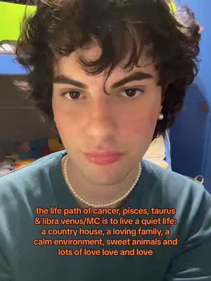 A young man with curly dark hair and light skin is centered in a selfie. He wears a teal sweater and a pearl necklace. Text overlays at the bottom.
