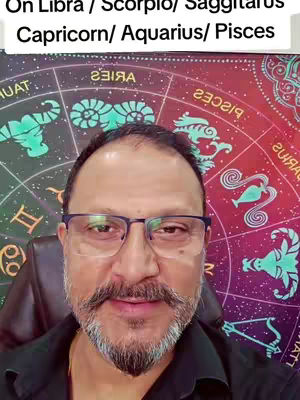 A selfie-style video where a man with glasses and a trimmed beard is seated in front of a background that appears to be a celestial design. Text overlaid on the image lists various zodiac signs.