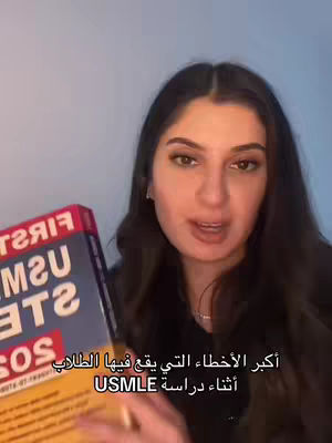 A woman with long dark hair is holding a book and talking to the camera, against a light blue background. Text in Arabic is overlaid. The image is well-lit, with a focus on the central figure.