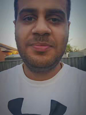 A selfie-style shot with a man in a white t-shirt. The background includes a house and fence, indicating an outdoor setting.
