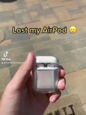 A hand holding a charging case for Apple AirPods. The background is a blurry outdoor setting, likely a patio or sidewalk. Overlay text in yellow font states, "Lost my AirPod", with an emoji.