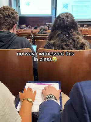 The cover image shows a classroom setting. Two people are in the foreground: one with a gold watch and one with a silver watch. Both people are holding papers. In the background, other students and the teacher are present.