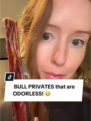 A close-up shot features a woman with fair skin and red hair looking directly at the camera with wide, inquisitive eyes. She appears to be holding a long, brown object resembling a dog treat near her face. A white text box overlies the image, containing text. The background isn’t well-defined, but the focus is on the woman and the object she is holding.
