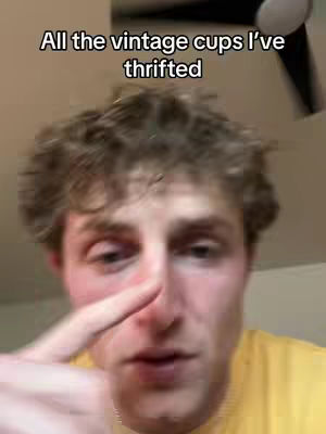 A man with short, curly brown hair is the primary focus, with a close-up on his face. He is pointing his index finger towards the screen, and the background is a softly lit, neutral-toned room, with a ceiling fan visible.