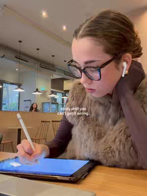 A woman with glasses is sitting at a table with a tablet and stylus pen. The background indicates a cafe setting. Text overlayed reads 'study until you can't get it wrong.'