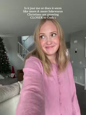 A woman is in front of the camera with a soft smile, wearing a pink button-down shirt. Text elements are overlaid on the image, the background is a living room showing glimpses of a staircase, a Christmas tree and decorations.
