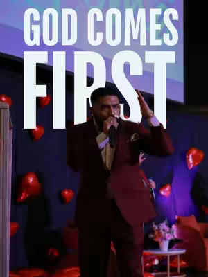 The cover image features a man in a maroon suit speaking into a microphone on a stage. Above him, large white text reads "GOD COMES FIRST". The background consists of purple and black hues, with red heart-shaped decorations.
