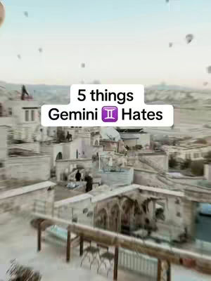 An aerial view of a city with light-colored buildings, possibly in Cappadocia, Turkey. The image includes a text overlay with the title '5 things Gemini Hates'. The sky is a gradient of light blue and white, with hot air balloons in the distance, suggesting a dawn or dusk setting.