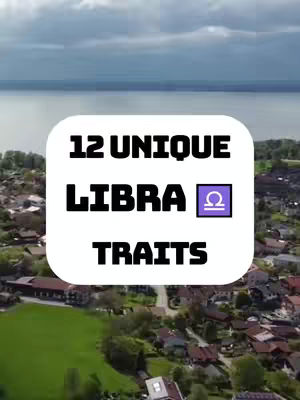 The cover image displays a scenic, aerial view of a town nestled beside a lake or sea under a cloudy sky. A white, rounded rectangle in the center prominently features bold, black text that reads "12 UNIQUE LIBRA TRAITS". Inside the word "LIBRA" is the Libra zodiac symbol in a purple box.