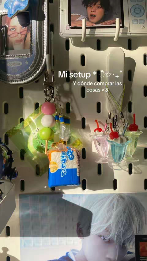 The image displays a white pegboard with various colorful charms and small photos attached. The charms include miniature ice cream sundaes, colorful round candies, and a small pack of bread. The background is a collection of items hanging on a white panel, including a photo of a person, giving the impression of a curated, personal setup.