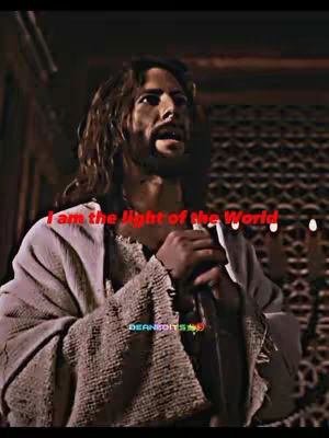 The image shows a man with long brown hair and a beard, dressed in light-colored robes, likely representing Jesus. Text in red overlayed across the image reads, "I am the light of the World". The lighting suggests an indoor setting with a dark background.