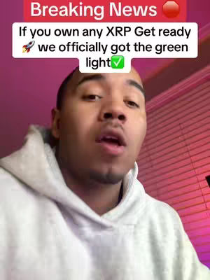 A man in a gray hoodie is centered, looking at the camera with his mouth slightly open. Above him, in a red banner, is white text that reads "Breaking News" with a red circle emoji. Below, overlaid text states, "If you own any XRP Get ready," followed by a rocket emoji and the text "we officially got the green light" with a green check mark.