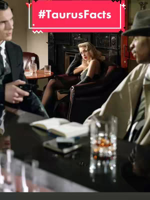 The image depicts a scene in a dimly lit setting, possibly a bar or lounge. Three people are present: a man on the left in a suit appears to be holding a gun. A woman in a black outfit sits in a large chair facing toward the right of the image. A man in a fedora and trench coat is standing on the right side of the image. The background includes a fireplace, liquor bottles and glasses on the bar, and a table where some of the individuals may be sitting. A text overlay indicates the hashtag #TaurusFacts.