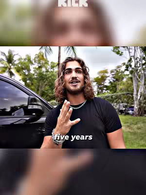 A man with long, wavy hair is standing outside near a black car, gesturing with his hand. Text stating "five years" is overlaid onto the image.