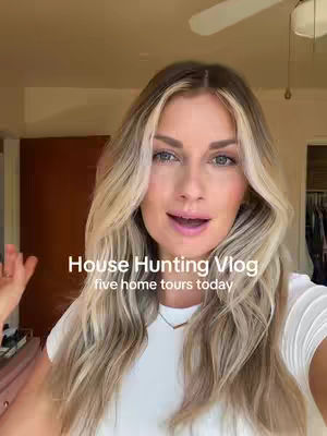 A woman with long blonde hair and a white t-shirt is the focal point, positioned slightly off-center. Behind her is a blurred interior setting, including a closed brown door. White text overlays read 'House Hunting Vlog' and 'five home tours today.' The color palette is warm, with natural lighting.