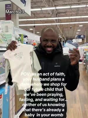 A man in glasses smiles, holding a baby outfit and a pack of baby items in a store. Text overlays state the date and a POV message.