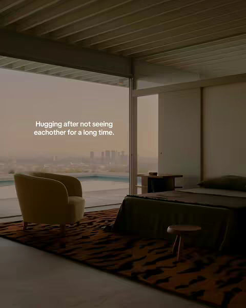 An interior shot of a modern room with a large window overlooking a cityscape. An armchair sits in the foreground, and a bed is partially visible. Text overlayed says, 'Hugging after not seeing eachother for a long time.'