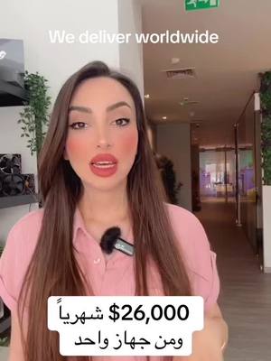 A woman with long brown hair wearing a pink shirt stands in front of a blurred background. The text overlayed on the image reads "We deliver worldwide" at the top and "$26,000 monthly from one device" in Arabic and English near the bottom. A microphone is attached to the woman's shirt.