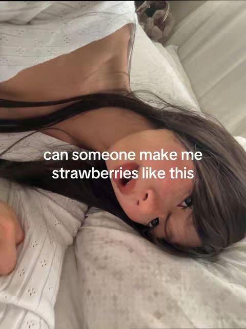 A woman is seen lying in bed, looking directly at the camera with a slightly open mouth. There is overlay text on the image. The woman has long dark hair, and she is resting on a white pillow and sheets.