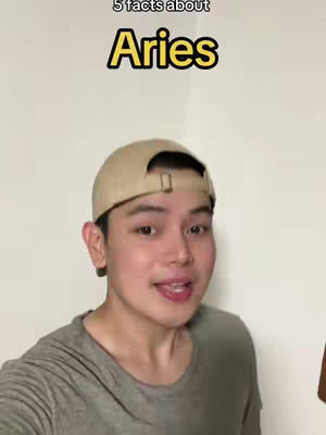A man wearing a baseball cap is centered in the frame, smiling slightly. Above him, text reads "5 facts about Aries" in a yellow outlined rectangle. The background is a plain white wall.