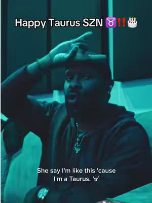 A man with dark skin is the primary subject, captured from the chest up. He appears to be indoors, with a teal-colored wall or background, creating a cool ambiance. Overhead, text reading 'Happy Taurus SZN' is displayed in white, with overlaid emojis signifying birthday or seasonal celebration. Further down; the man in the foreground, with a hand casually resting near his head, is looking forward as though speaking. A necklace, watch and hat are visible. The video's bottom section overlays, 'She say I'm like this 'cause I'm a Taurus.'
