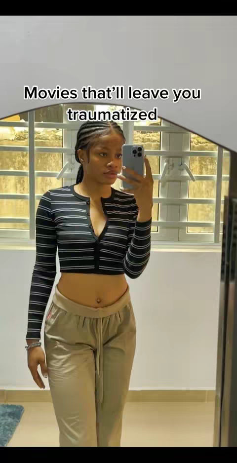 A woman is seen in a mirror taking a selfie, the text overlayed reads "Movies that\'ll leave you traumatized". She is wearing a striped shirt, and light-colored trousers.
