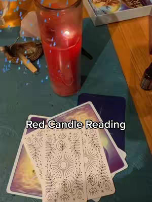The image shows a top-down view of a table setup for a spiritual or divination session. A tall red candle burns brightly in a clear glass, positioned in the center. Arranged around it are several tarot cards, their backs facing up, showing a purple and gold gradient design. The card at the front of the deck displays intricate white line drawings. A small container with a lid, a small golden object that looks like a key and some crystals are placed to the left of the candle. The surface beneath everything is a teal color. The text overlay at the bottom says 'Red Candle Reading'.
