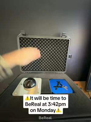 The cover image shows a case with a black top, a black surface, a metal plate with a round black object, and another plate with blue and white icons, and the time and date displayed in white text. A hand appears blurred in the upper left.
