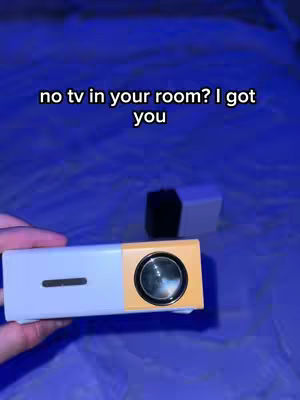 The image showcases a close-up of a white and yellow projector held in a hand. Above the projector, text reads 'no tv in your room? I got you'. The background has a blue gradient.