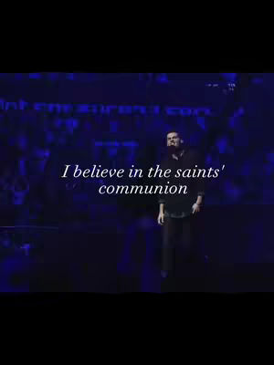 The image shows a man standing on a stage with text overlayed on the image. The majority of the cover art is dark and blueish with an audience in the background. Text overlay reads 'I believe in the saints' communion'.