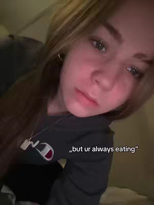 A close-up shot of a young woman with long, light brown hair. The woman is looking downward with a slightly melancholic expression. She is wearing a dark gray hoodie with a white and red logo. The background is dimly lit, suggesting a bedroom or indoor setting. Text overlayed on the cover image says, "but ur always eating".