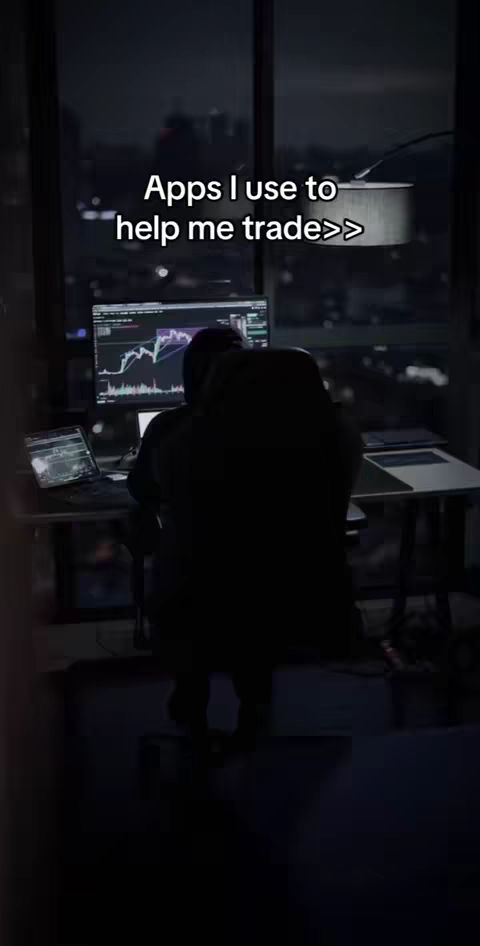 A dark, nighttime scene with a silhouetted figure seated at a desk. A large computer monitor displays what appears to be a financial chart. A smaller screen lies to the left, showing more data. The background reveals a cityscape through a large window, with soft lights suggesting buildings. On the top center, overlayed text. The lighting is dim, with a focus on the screens.