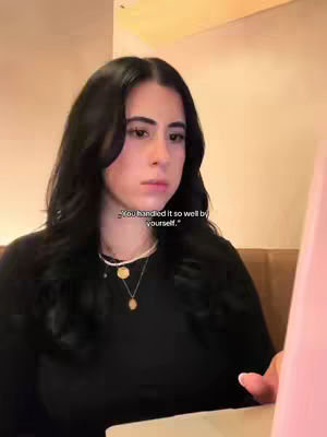 A young woman is seated, angled slightly, in front of what appears to be a light-colored laptop. She has long, dark hair and is wearing a black top. The lighting is soft, giving a warm feel to the environment. A text overlay reads, You handled it so well by yourself.
