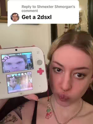 A selfie featuring a young woman holding a white 2DS console up with a Dexter theme playing on screen. She is positioned in front of a soft-focus background. The image features a speech bubble with text in the upper left corner.