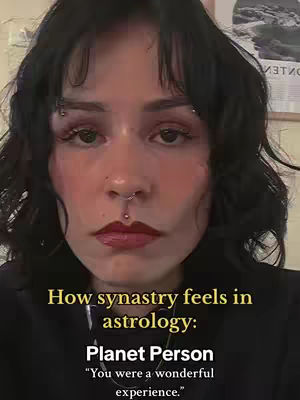 A close-up shot featuring a fair-skinned person with dark hair and multiple facial piercings. They have dark eye makeup, full lips, and are looking directly at the camera. Text overlays in a bold, sans-serif font provide context about synastry in astrology.