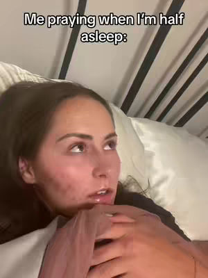 A woman is lying in bed, looking upward with a slightly concerned expression. The lighting is soft, suggesting a bedroom setting with bedsheets and pillows.