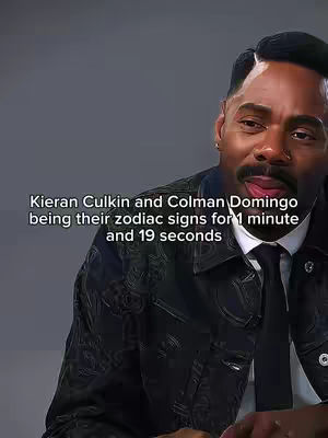 The image features a man with short, styled black hair, a neatly trimmed mustache and a goatee. He's wearing a black leather jacket over a white shirt and a black tie. The background is a solid grey. Text overlayed on the image reads, "Kieran Culkin and Colman Domingo being their zodiac signs for 1 minute and 19 seconds."